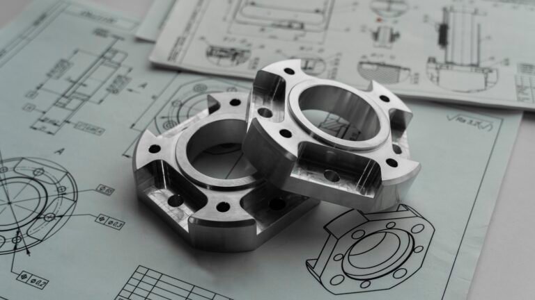 Two machined metal components resting on engineering drawings for prototype development