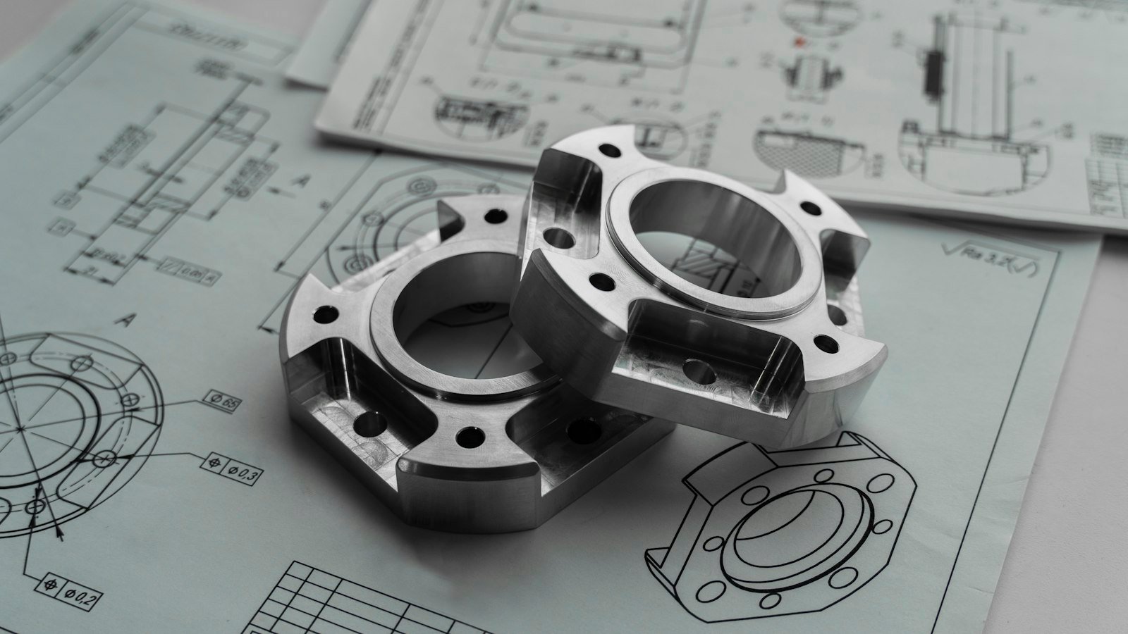 Two machined metal components resting on engineering drawings for prototype development